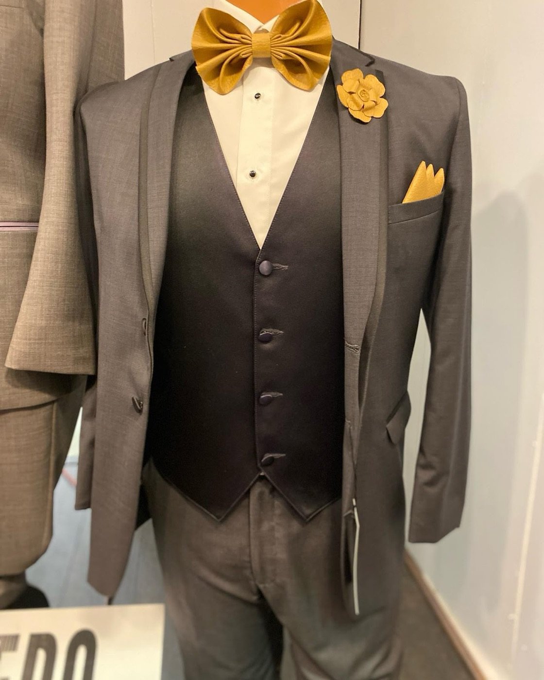 A charcoal three-piece tuxedo with a gold bow tie and pocket square